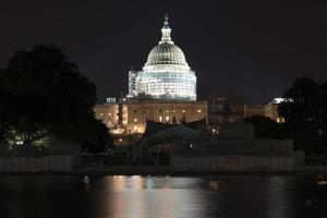 The US Capitol Building under scaffolding as seen across the reflecting pool at night in Washington, DC. photo