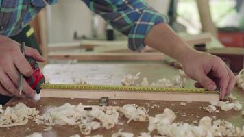 el dueño de un hombre asiático, un pequeño negocio maderero, está preparando madera para la producción de muebles. el carpintero está ajustando la superficie de la madera al tamaño deseado. concepto de carpintero y propietarios de pequeñas empresas. video