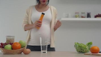een gelukkig moeder is dansen in de keuken gelukkig gieten oranje sap in een glas.a zwanger vrouw drinken oranje sap voor is gestegen vitamines naar baby. gezond zwanger vrouw concept. video