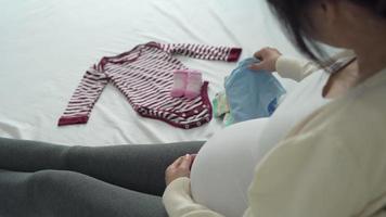 Schwangere Frauen wählen Kleidung aus, nachdem sie sie gereinigt haben, um sich auf ihre Kinder vorzubereiten. Mütter überprüfen die Tücher nach dem Online-Kauf erneut. neugeborenes und schwangeres konzept.