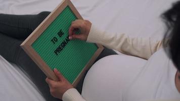 mujeres embarazadas escribiendo para estar embarazadas en el tablero verde. la mujer está preparando una tabla para tomar una foto y publicarla en las redes sociales mostrando su embarazo. concepto de madre feliz. video