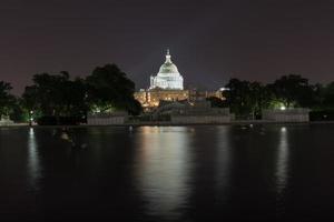 el edificio del capitolio de estados unidos bajo andamios como se ve a través de la piscina reflectante en la noche en washington, dc. foto