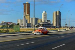 la habana, cuba - 15 de enero de 2017 - coche clásico conduciendo por el malecón con la casa de las américas al fondo en la habana, cuba. foto