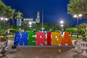 letras grandes y coloridas que representan a Mérida con una icónica catedral de Mérida al fondo por la noche. foto