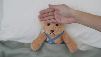 concepto de sentirse enfermo y fiebre. utilizando un oso como representación infantil. los hombres miden la temperatura de la cabeza con las manos y usan un gel refrescante para reducir la fiebre.