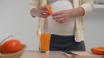 Eine schwangere Frau entsaftet Orangensaft, um ihr ungeborenes Kind mit Vitaminen zu versorgen. Schwangere machen ihren eigenen Orangensaft, indem sie die Orange kaufen und den Saft 100 Prozent pur auspressen. gesund schwanger