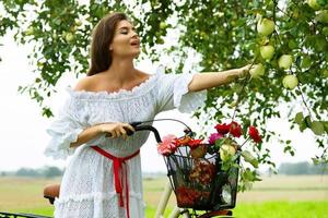 Woman on the bicycle is picking fresh apples from the tree in the village garden photo