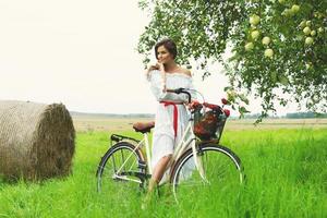 Woman on the bicycle is picking fresh apples from the tree in the village garden photo