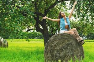 Happy woman wearing denim vest is sitting on the haystack photo