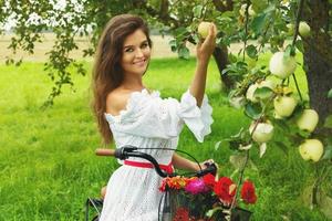 mujer en bicicleta está recogiendo manzanas frescas del árbol en el jardín del pueblo foto