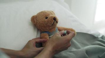 concepto de sentirse enfermo y fiebre. utilizando un oso como representación infantil. los hombres miden la temperatura de la cabeza con las manos y usan un gel refrescante para reducir la fiebre. video