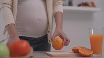 Pregnant woman was picking an oranges and using a knife for cut the orange and make orange juice. Fresh orange juice helps mothers feel fresh and provides vitamins for the unborn child.