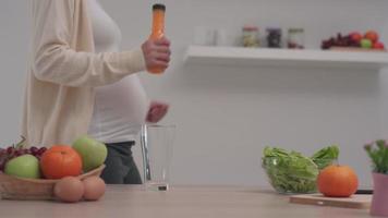 Lycklig gravid kvinna innehav orange juice och dans i de kök. dryck frukt juice tillhandahåller en vitamin lyft för gravid kvinnor och foster. begrepp av kropp underhåll för gravid kvinnor. video