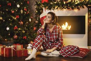 mujer feliz sentada al lado de la chimenea en decoraciones navideñas foto