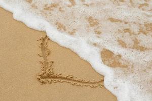 Drawing of a heart shape on the sand and wave with foam photo