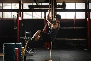 Sportsman doing rope climbing exercise in cross training gym photo