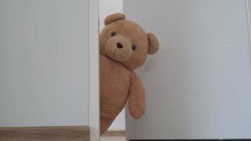 Konzept für Kind. ein brauner Teddybär streckte sein Gesicht hinter der Wand hervor. der braune teddybär stupst ein gesicht neben der tür das gesicht des teddybären schaut lächeln. Teddybär im Zimmer versteckt.
