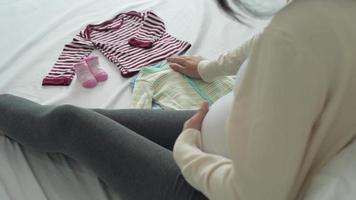 as mulheres grávidas tocam nas roupas depois de limpá-las para se preparar para os filhos. as mães estão escolhendo roupas para cada faixa etária. conceito de recém-nascido e grávida. video