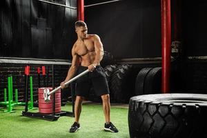 Man is hitting tire with a sledgehammer during his cross training workout photo