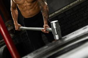 Man is hitting tire with a sledgehammer during his cross training workout photo