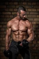 Bodybuilder doing exercises with dumbbells against brick wall photo