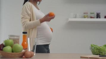 una mujer embarazada de buen humor está felizmente usando una cocina. las mujeres embarazadas preparan naranja para jugo de naranja. naranja mucha vitamina c para embarazadas y bebés. video