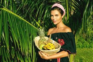 mujer joven feliz con una cesta llena de frutas exóticas foto