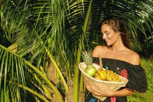 mujer joven feliz con una cesta llena de frutas exóticas foto