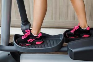 Female legs on a elliptical trainer in the gym photo