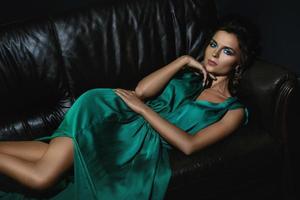 mujer sexy con un hermoso vestido verde posando en un sofá de cuero
