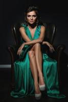 Woman wearing beautiful green silk dress is posing on leather couch photo