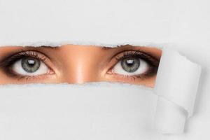 Young female eyes looking through torn paper photo