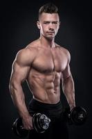 Young man bodybuilder doing exercises with dumbbells photo