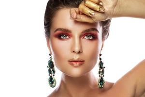 Beautiful woman with a colorful makeup is wearing earrings with green emeralds photo