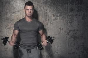 joven culturista haciendo flexiones de bíceps con pesas foto