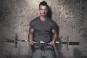 Young bodybuilder with barbell in against cocnrete wall photo