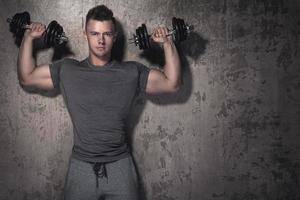 Young bodybuilder is doing overhead press exercise photo