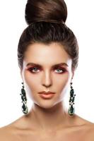 Beautiful woman with a colorful makeup is wearing earrings with green emeralds photo