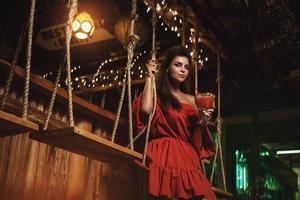 Charming woman wearing red dress in evening summer bar photo