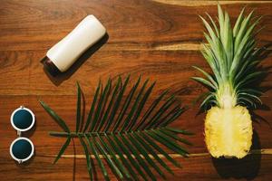 Flat lay of Sunscreen, sunglasses and pineapple fruit photo