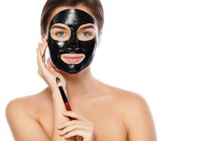 Beautiful woman is applying purifying black mask on her face photo