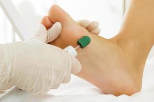 Pedicure master work. Closeup of female feet and hands in gloves with a special machine tool. photo