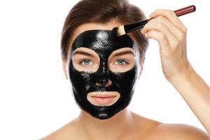 Beautiful woman is applying purifying black mask on her face photo