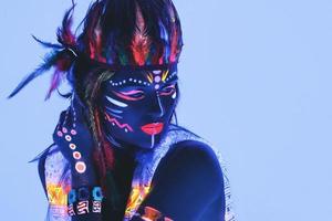 Model in image of Native american with neon makeup, which made of fluorescent paint in ultraviolet light. photo