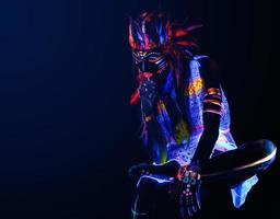 Model in image of Native american with neon makeup, which made of fluorescent paint in ultraviolet light. photo