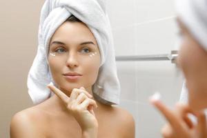 Woman using moisturizing and anti-aging cream under her eyes photo