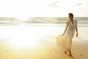 una mujer con un hermoso vestido blanco camina por la playa al atardecer foto