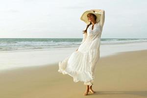 Woman wearing beautiful white dress is walking on the beach during sunset photo