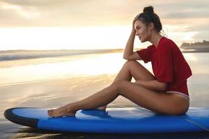 Woman sitting on surfboard on the beach after her surfing session photo