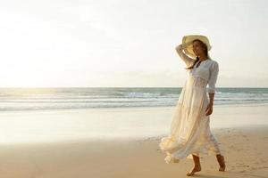 una mujer con un hermoso vestido blanco camina por la playa al atardecer foto